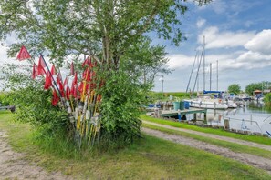 A riverside area with boats docked, a tree with red flags, and a clear sky.