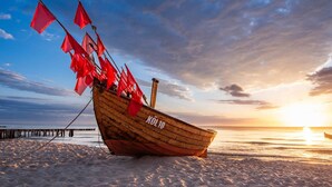 A wooden boat with red flags on a sandy beach at sunset. - Vacation home Nordhorn - your cozy home in Koserow on the Baltic Sea (Ostseebad Kölpinsee)