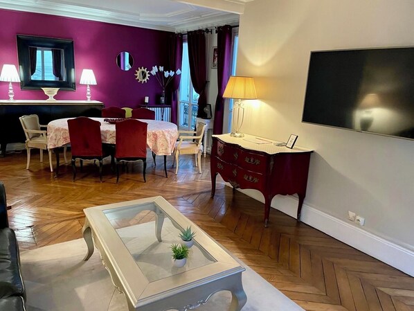 A living room with a dining area, a TV mounted on the wall, and a staircase leading to an upper floor.