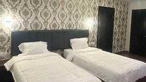 A hotel room with two beds, patterned wallpaper, and a dark headboard.