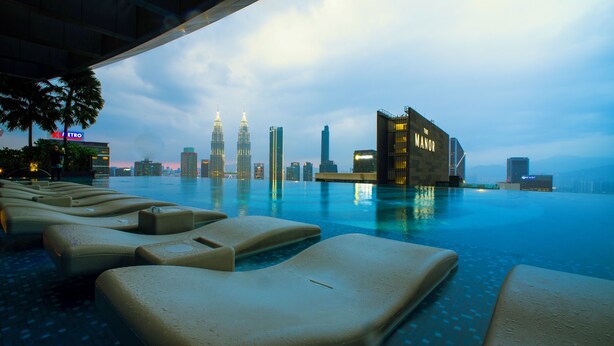 Ein Infinity-Pool mit Liegestühlen und Blick auf den Stadtpanoramahimmel, mit einem Gebäude, das 'The Manor' heißt.