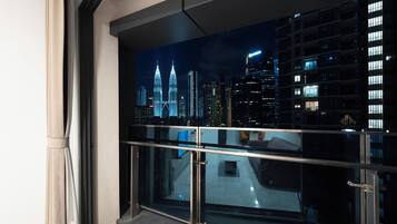 A view from a balcony with a glass railing, overlooking a cityscape at night with illuminated buildings.