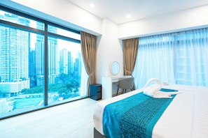 A modern hotel room with a large window, a bed with a blue patterned bedspread, a desk with a chair, and a mirror. - Moonway Luxury Suites At Eaton Residence (Kuala Lumpur)