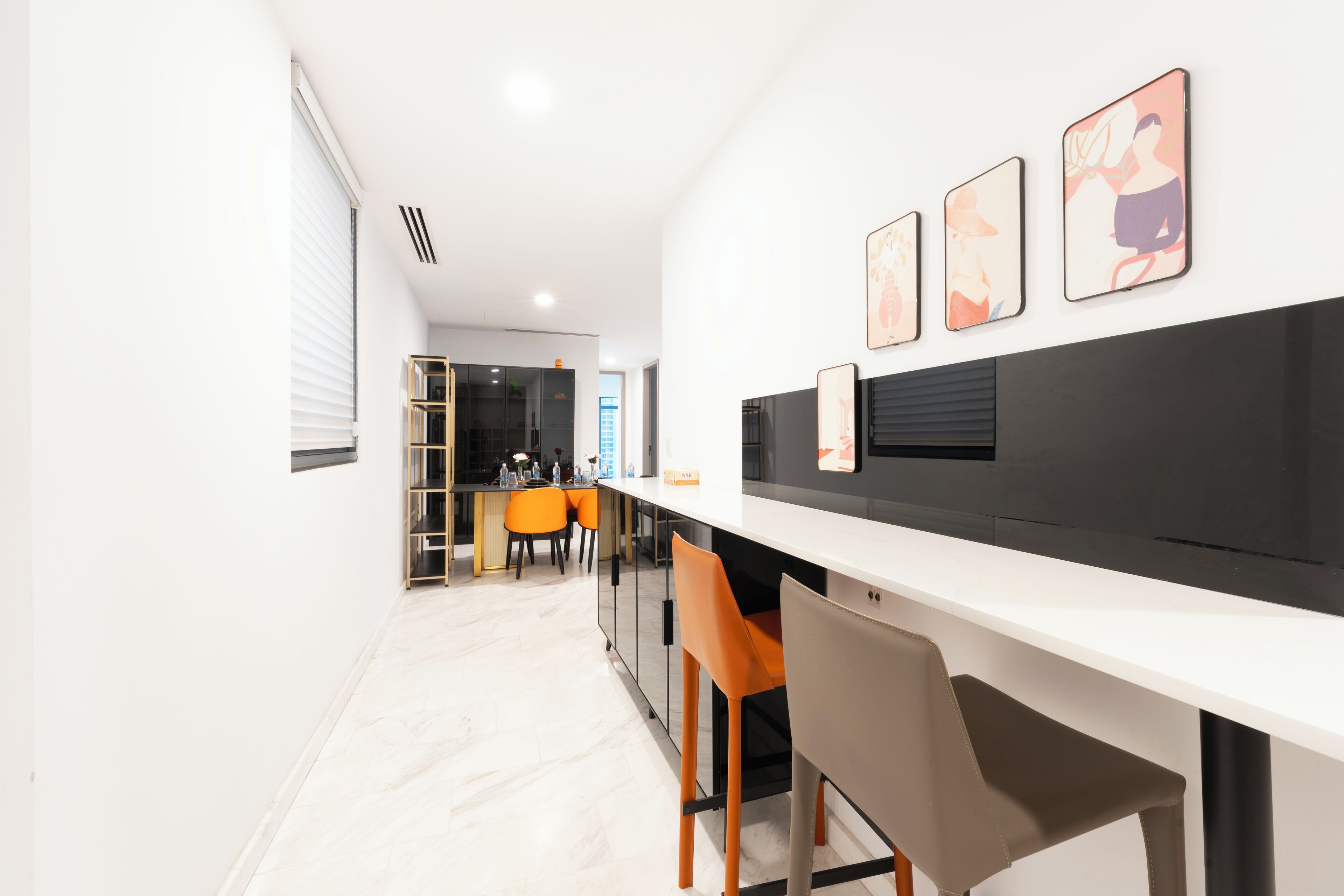 A modern kitchen with a white countertop, orange chairs, and a black backsplash.