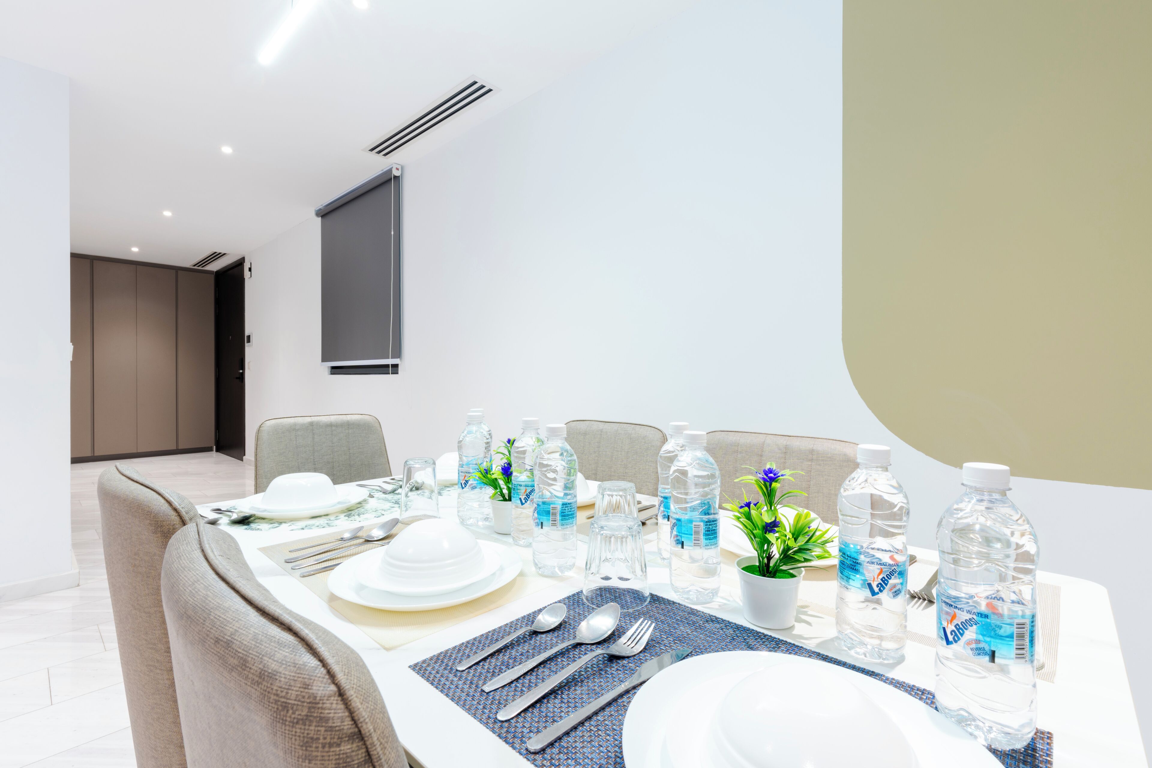 Un coin repas avec une table dressée pour quatre personnes, comprenant des bouteilles d’eau, des couverts et une plante en pot.