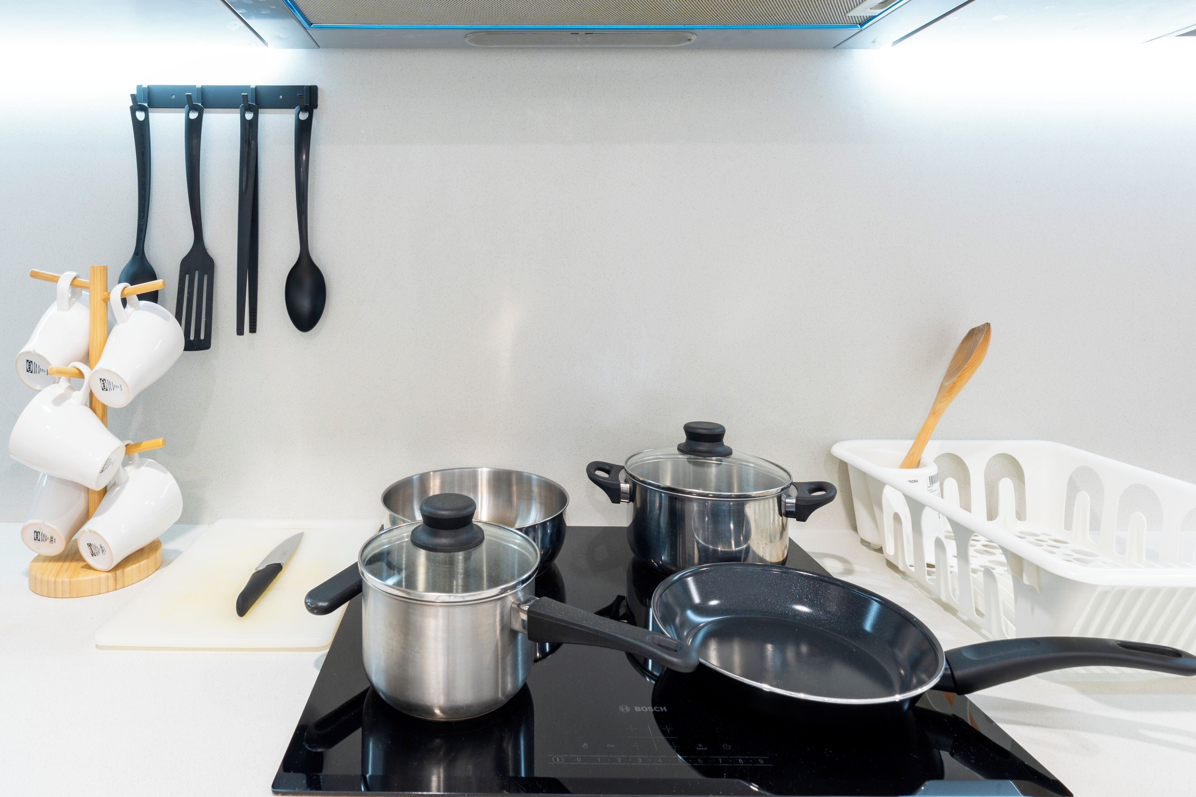 Una cocina con estufa, ollas, tabla de cortar y utensilios.