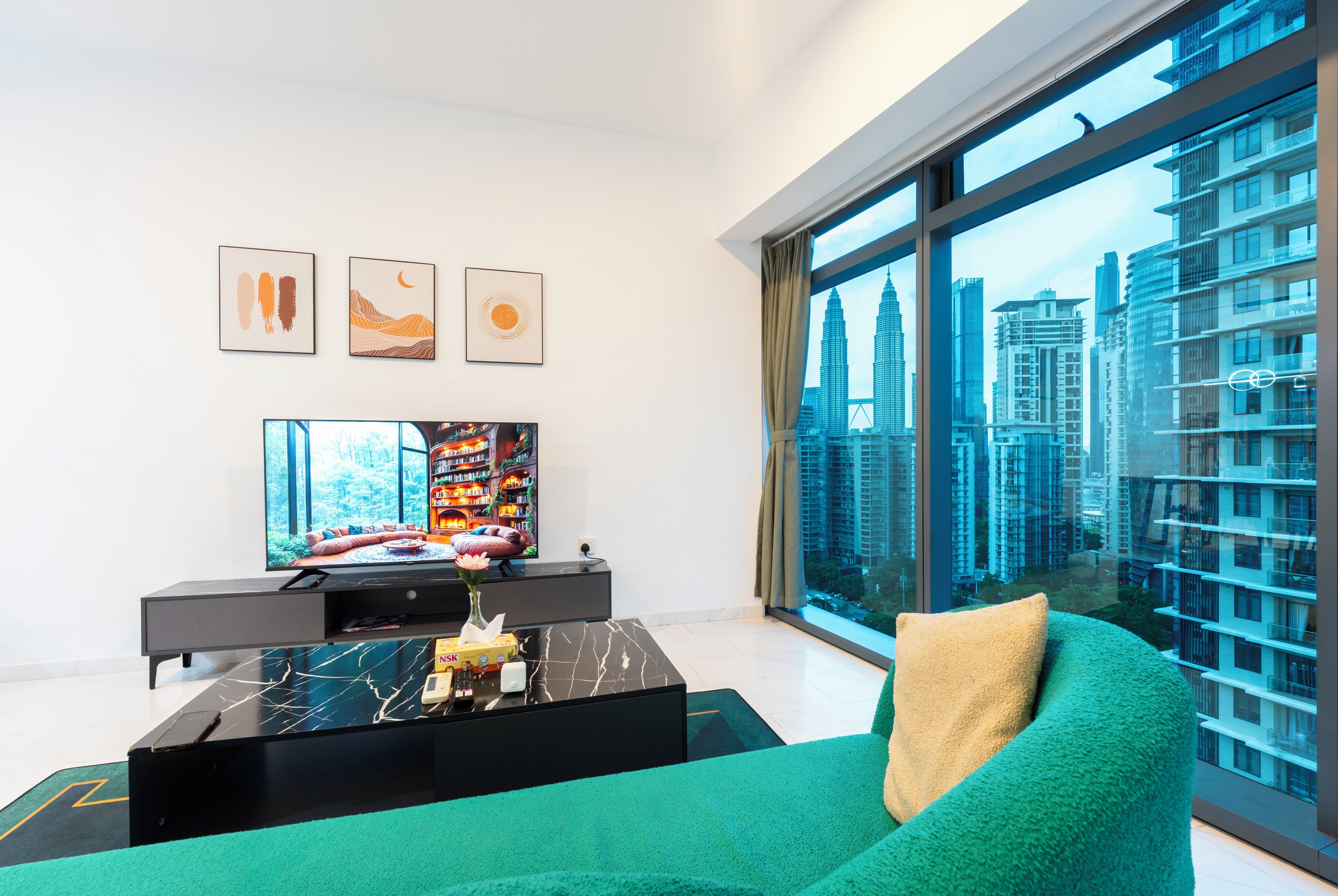 A modern living room with a large TV, artwork on the wall, and a view of a cityscape through large windows.