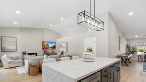 A modern kitchen with a central island, a dining area with a wooden table, and a living room with a sofa and a TV. - Private Pool, Hot Tub & Putting Green Home (Scottsdale)