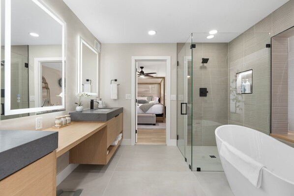 A modern bathroom with a glass shower enclosure, a freestanding bathtub, and a vanity with a mirror.