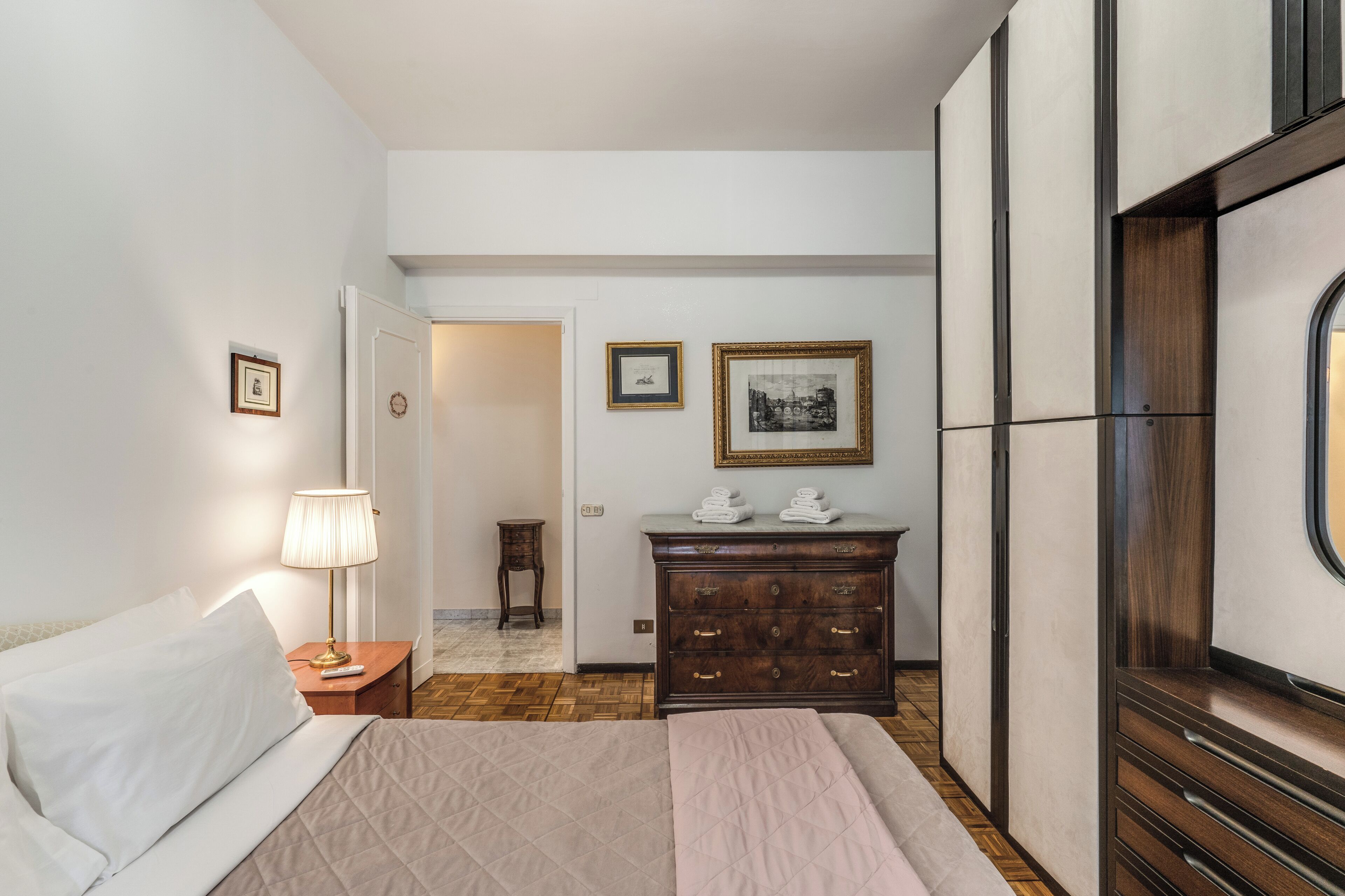Une chambre d’hôtel avec un lit, une table de chevet avec une lampe, une commode et des tableaux encadrés au mur.