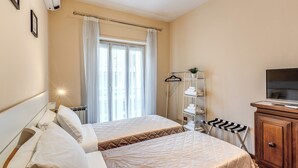 A hotel room with two beds, a TV, a wardrobe, a radiator, and a window with curtains. - Musei Vaticani Apartamento per 8 persone (Rome)