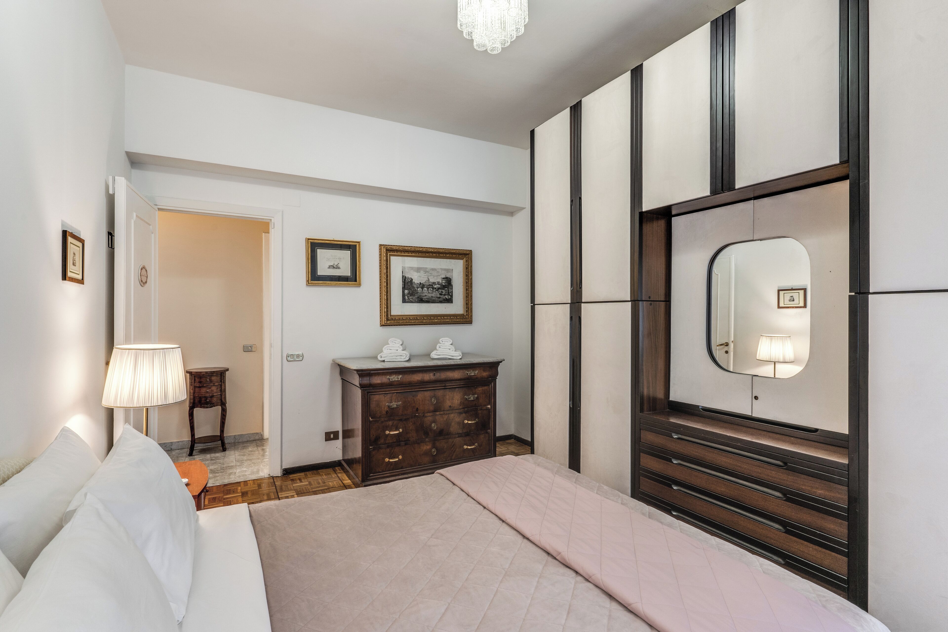 A hotel room with a bed, a dresser, a mirror, and a door leading to another room.