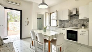 Een moderne keuken met witte kastjes, een betegelde achterwand en een eethoek met tafel en stoelen.