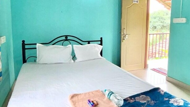Un lit simple avec un matelas et des oreillers blancs, une couvre-lit à motifs floraux bleus et une petite table sur laquelle se trouvent une bouteille et une boîte de mouchoirs.