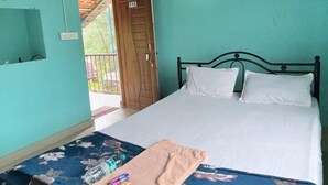 Une pièce avec un lit, une table recouverte d’une nappe à motifs floraux et une porte donnant sur l’extérieur.