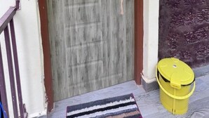 Une porte en bois avec une plaque portant le numéro « 113 », un seau jaune et un tapis rayé sur un plancher en bois.