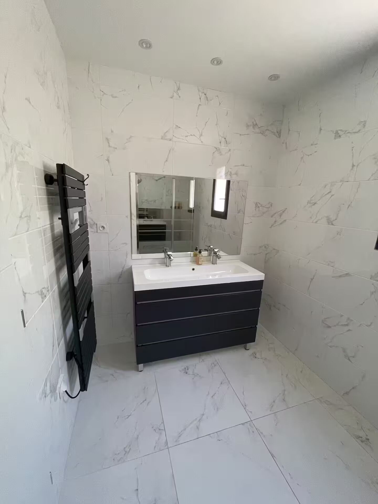 A modern bathroom with a large mirror, a white sink, and a black vanity.