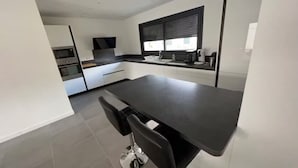 Una cucina moderna con un piano di lavoro scuro, mobili bianchi e una finestra con persiane.
