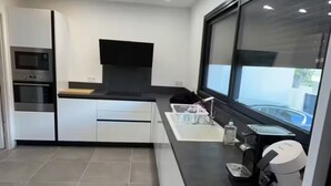 Una cucina moderna con mobili bianchi, forno integrato e un'ampia finestra con vista su una piscina.