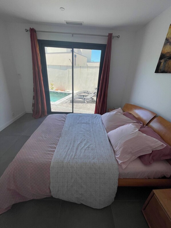 A bedroom with a bed, a view of a swimming pool, and a balcony.