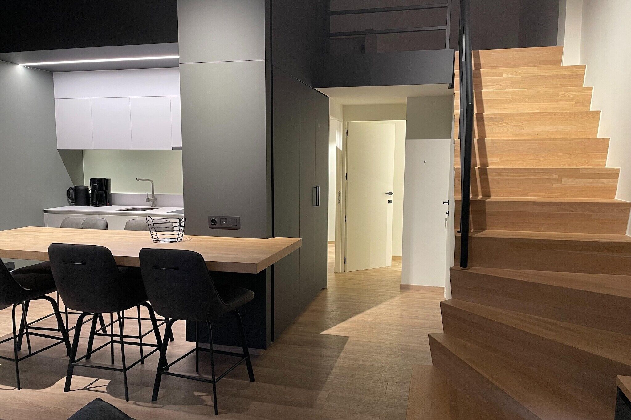 Eine moderne Küche mit einer Holzinsel, schwarzen Stühlen und einer Treppe mit Holzboden.