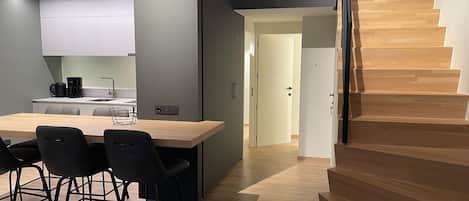 Eine moderne Küche mit einer Holzinsel, schwarzen Stühlen und einer Treppe mit Holzboden.
