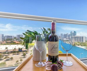 A balcony with a wine bottle and glasses, a potted plant, and a city view.