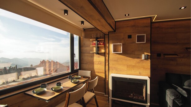 Een modern interieur met een eethoek, open haard en grote ramen met uitzicht op de bergen.