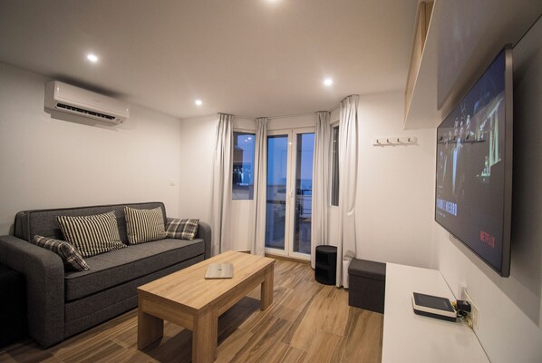Un salón moderno con un sofá gris, una mesa de centro de madera y un televisor montado que muestra la interfaz de Netflix.