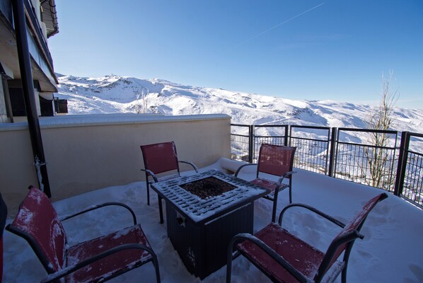 Un balcón con mesa y sillas, con vistas a un paisaje montañoso nevado.