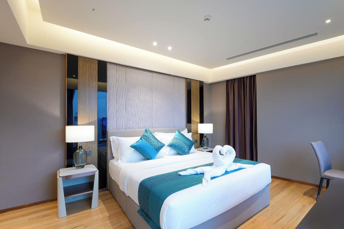 Une chambre d’hôtel moderne avec un grand lit, deux tables de chevet, une chaise et une vue sur le paysage urbain.