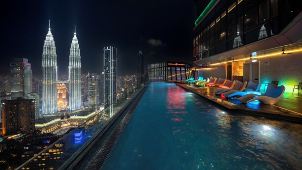 Zona de piscina con vistas a las Torres Petronas, sillones modernos y barandilla de vidrio.