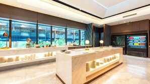 Un vestíbulo de hotel moderno con un mostrador de recepción de mármol, un amplio ventanal con vistas a zonas verdes y una máquina expendedora.
