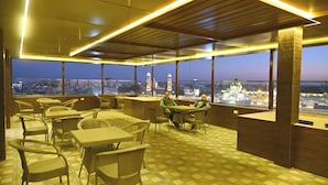A rooftop terrace with wicker furniture, large windows offering city views, and a checkered floor pattern.