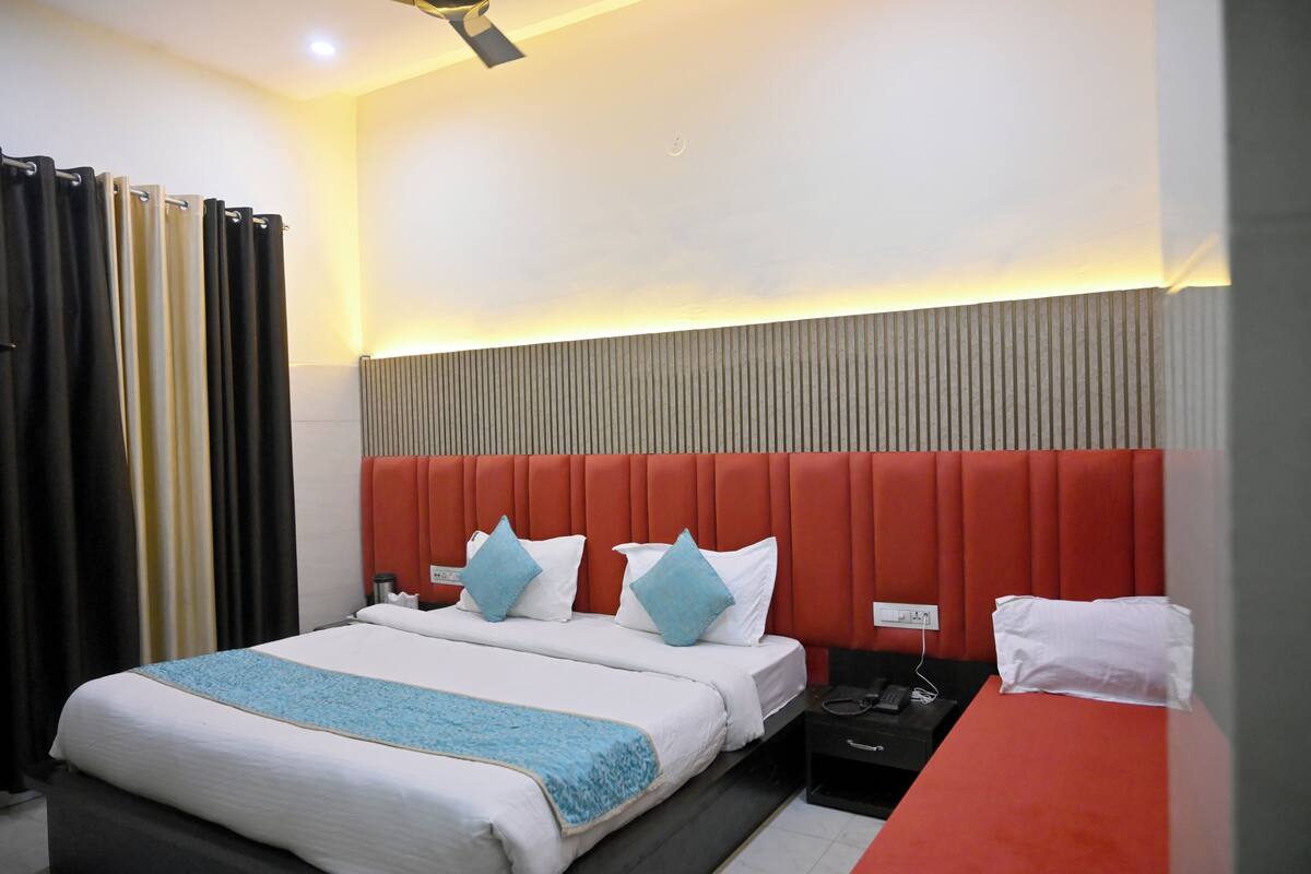 A hotel room with a large bed, a red headboard, and a bedside table with a phone and charger.
