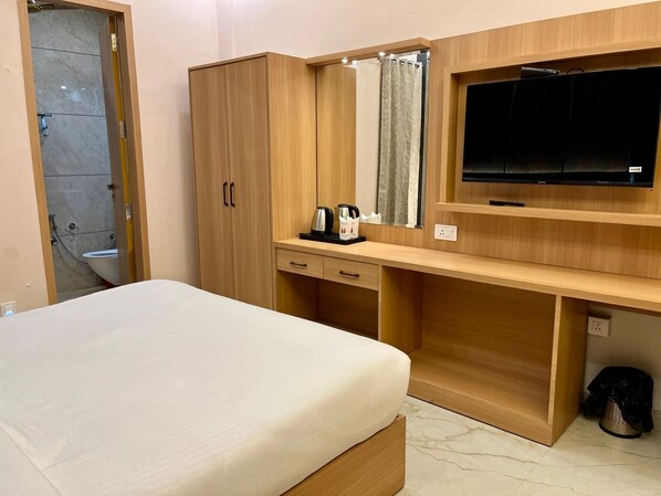 A hotel room with a bed, wooden wardrobe, a desk with a mirror, a television, and a shower area. - One Earth City Pearl Amritsar (Amritsar)