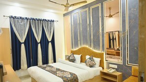 A well-lit bedroom with a large bed, a bedside table with a phone, and a mirror above the bed.