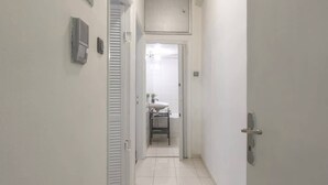 Un pasillo estrecho con paredes blancas y piso de baldosas que lleva a un baño con lavabo y espejo.