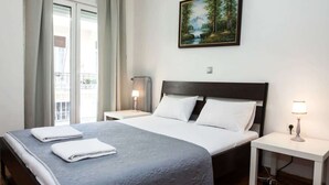 Habitación de hotel con cama, dos mesitas de noche, un cuadro y vistas a un balcón.