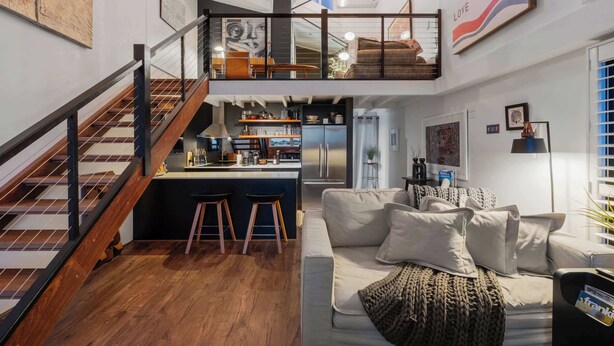 A modern interior with a staircase, a kitchen area, a living room with a sofa, and artwork on the walls. - Luxury Water Views ~ 2Bed/2Bath/1Car/Pool (Teneriffe)