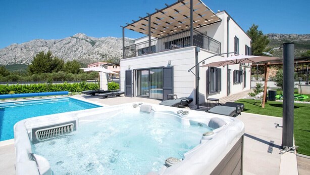 Ein modernes, zweistöckiges Haus mit Pool, Sitzgelegenheiten im Freien und Blick auf die Berge.