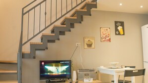 Un salon moderne avec un escalier en bois, un téléviseur à écran plat, une machine à café et une table à manger avec une chaise.
