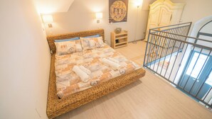 Une chambre avec un grand lit, une table de chevet en bois, une œuvre d’art accrochée au mur et un balcon doté d’une balustrade.
