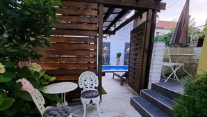 Een terras met stenen vloer, witte tuinmeubels en een houten pergola.