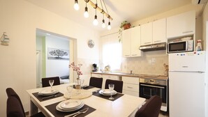 Een moderne keuken met witte kasten, een ingebouwde oven, een magnetron en een koelkast. Er staat een eettafel gedekt met borden, bestek en een vaas met bloemen.