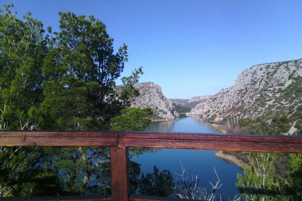 A wooden deck overlooking a calm lake with rocky cliffs and dense greenery.