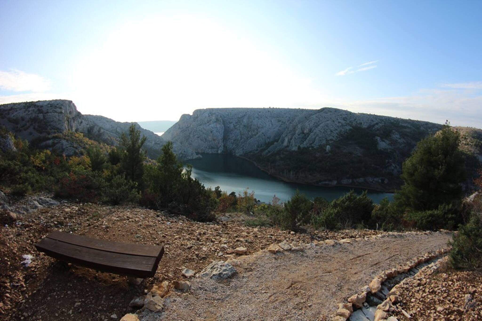Paesaggio roccioso con una panchina e vista su un lago circondato da montagne.