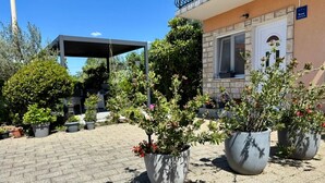 Un patio con plantas en macetas, una zona de estar cubierta y un edificio con fachada de piedra.