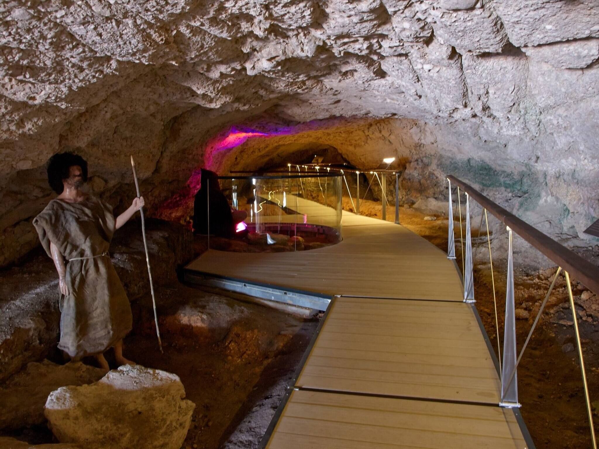 Eine Höhle mit einem Holzsteg und Metallgeländern, der zu einer Plattform mit einer Glaseinfriedung führt.