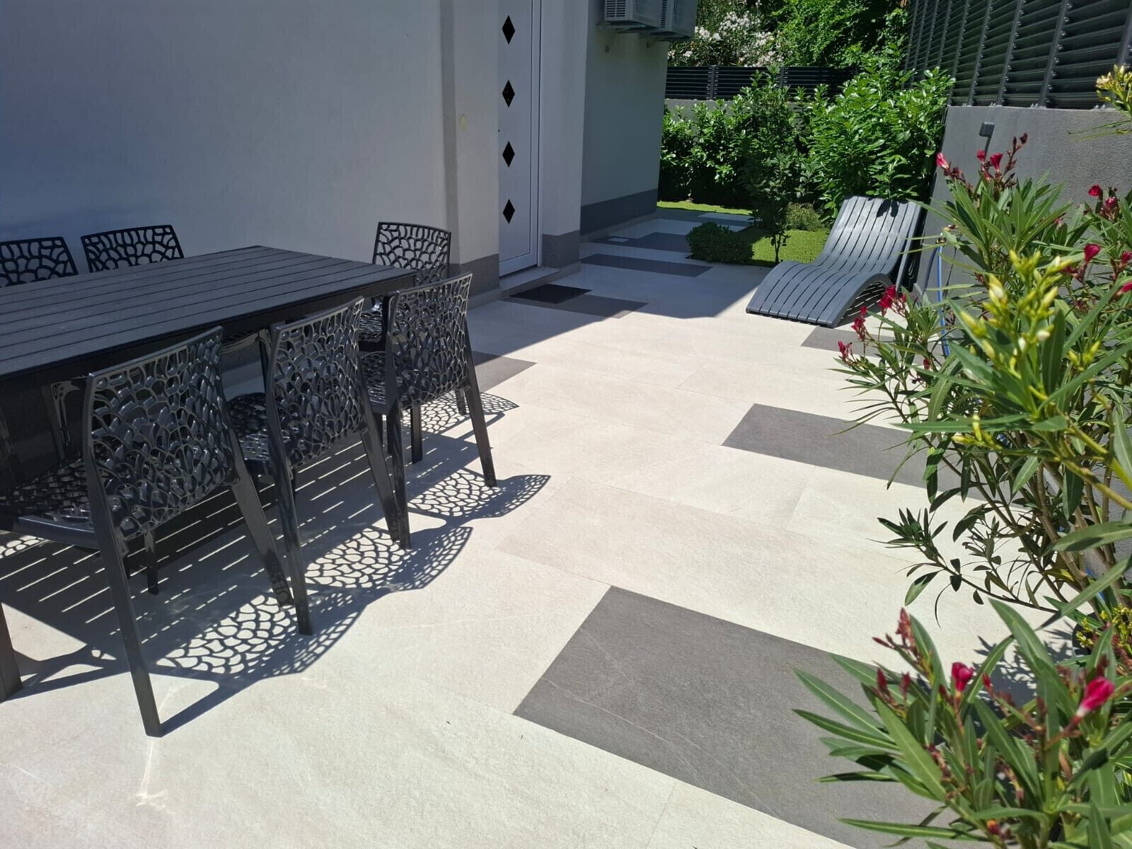 Une terrasse extérieure avec une table et des chaises, un petit jardin et un chemin menant à une porte.